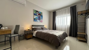 A modern hotel room with a bed, a desk with a chair, a small table with a coffee maker, a bedside table with a lamp, and a wardrobe. - Bayside (Marsaxlokk)