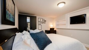 Et moderne hotelværelse med en stor seng, et skrivebord med lampe, et fladskærms-TV på væggen og billeder i rammer på væggen.