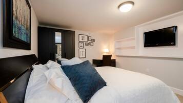 Une chambre d’hôtel moderne avec un grand lit, un bureau avec une lampe, un téléviseur à écran plat fixé au mur et des tableaux encadrés accrochés au mur.