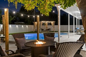 Une terrasse extérieure avec des meubles en osier, un foyer et des guirlandes lumineuses.