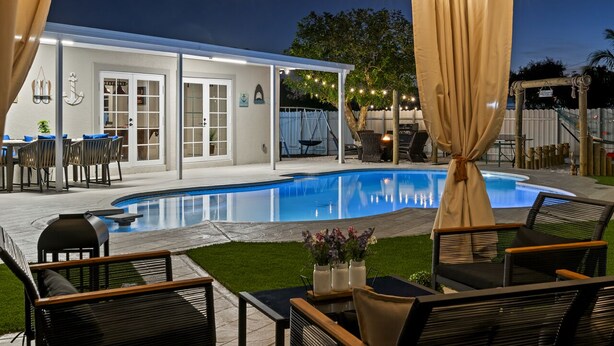 Un jardin avec une piscine, des meubles d’extérieur et des guirlandes lumineuses.
