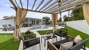 Une terrasse extérieure couverte avec une piscine, des chaises longues et un coin repas.