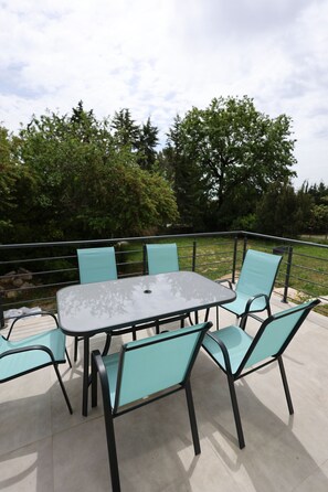 Eine Terrasse im Freien mit Tisch und Stühlen, umgeben von einem Metallgeländer.