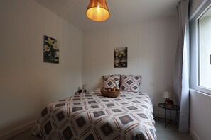 Ett sovrum med ett mönstrat sängöverkast, en hängande lampa och två tavlor som hänger på väggen.