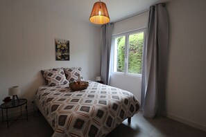 Une chambre à coucher avec une couvre-lit à motifs, une table de chevet avec une lampe, une fenêtre avec des rideaux et un luminaire suspendu.