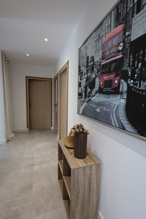 Ein Korridor mit einem Holzkonsolentisch, einer Blumenvase und einem großen Stadtbild an der Wand.