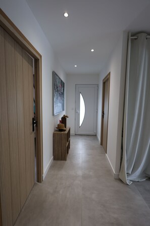 Un couloir avec une porte en bois, une petite table sur laquelle se trouve un chapeau, et un tableau accroché au mur.