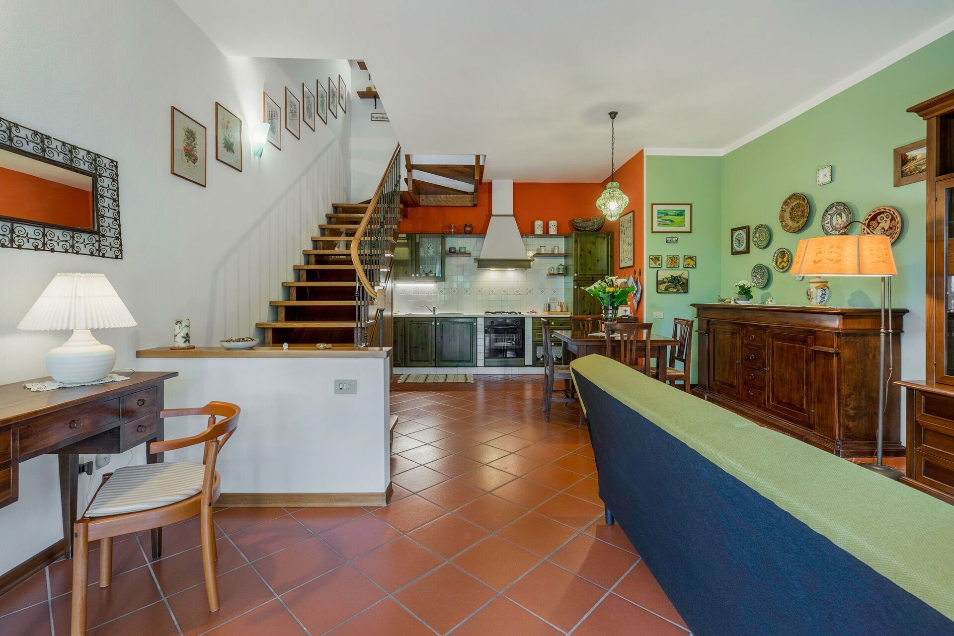 Ampla sala de estar com cozinha, área de jantar e escada que dá acesso a um andar superior.