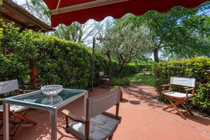 An outdoor patio with a glass table, two wooden chairs, and a red canopy. - Casa Bellosguardo in Vinci (Vinci)