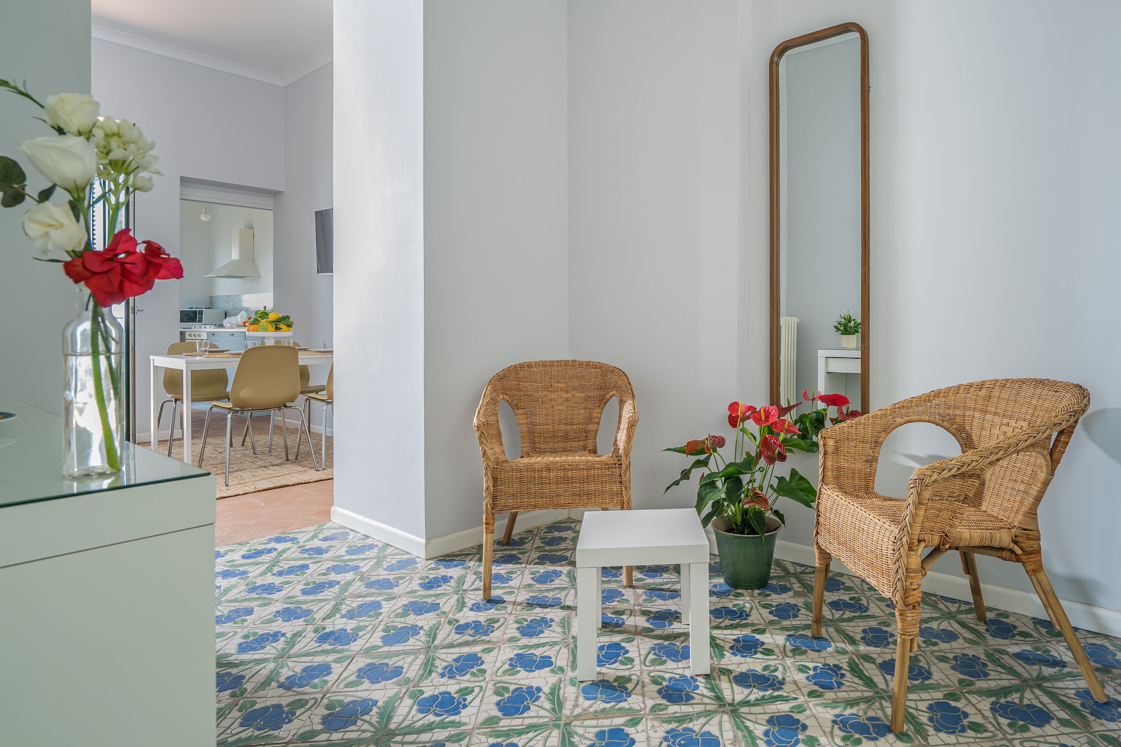 A room with a dining area, two wicker chairs, a small white table, and a mirror on the wall.