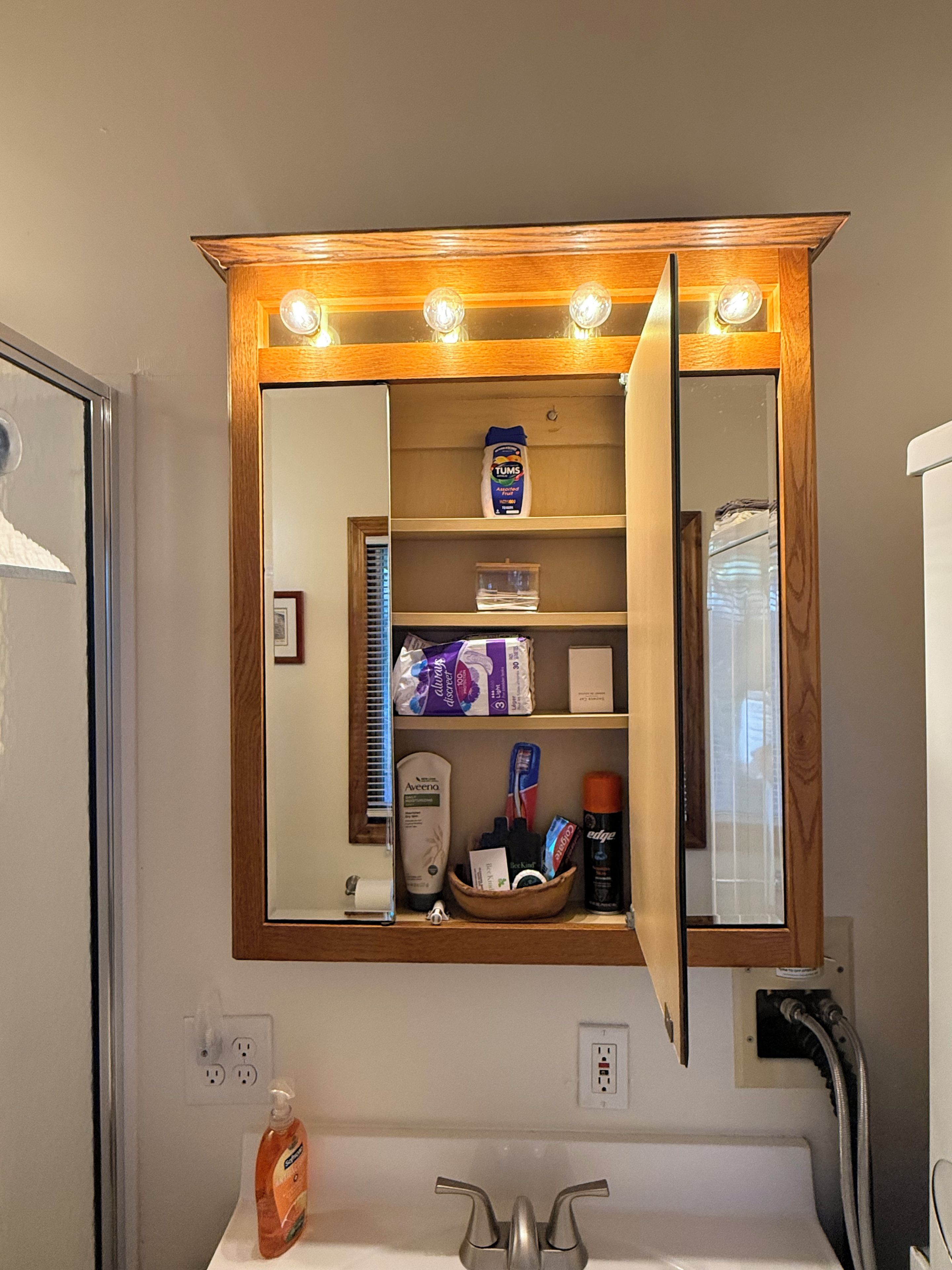 Un mueble de baño con espejo, luces sobre la cabecera y un estante con artículos de aseo.