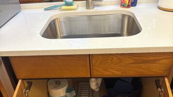 A kitchen sink with a window above it, a countertop with cleaning supplies, and a wooden cabinet below.