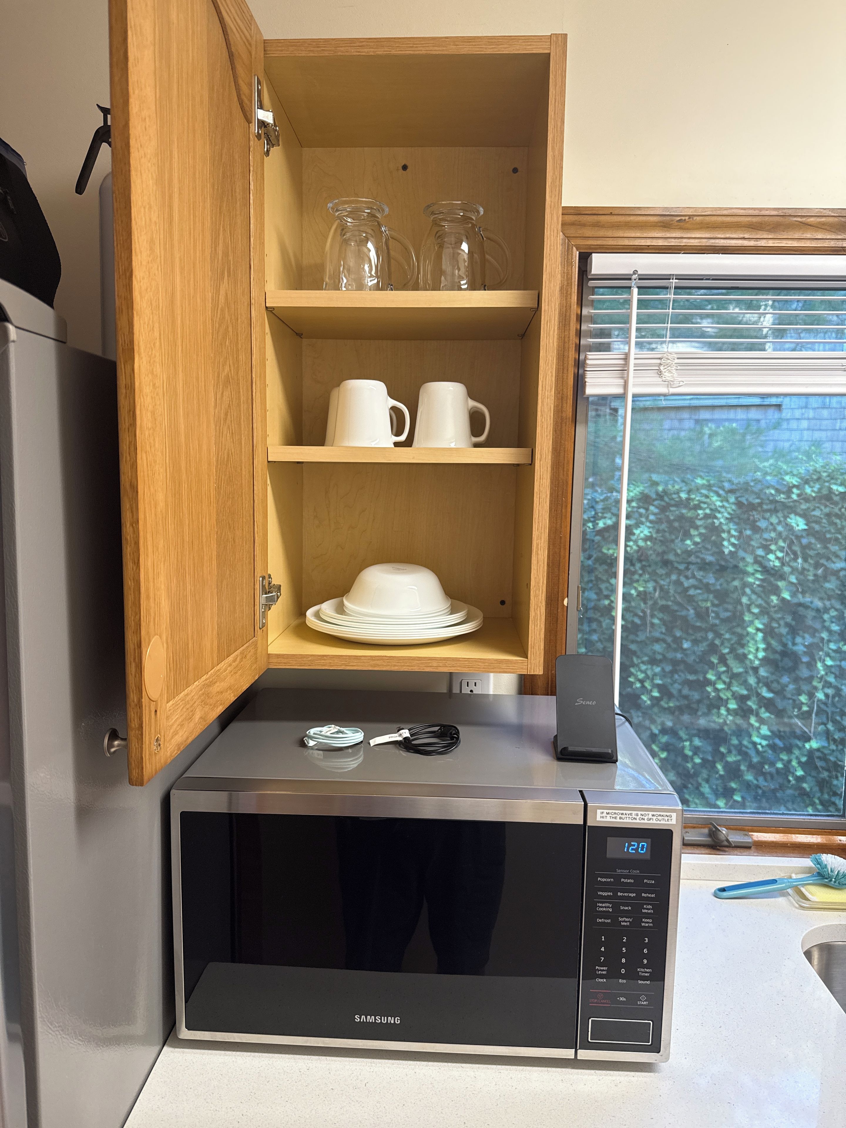 Une cuisine équipée d’un four à micro-ondes, d’un meuble contenant de la vaisselle et d’une fenêtre donnant sur la verdure.