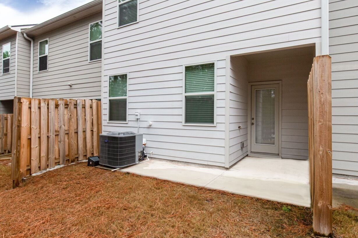 A residential building with a covered porch, a wooden fence, and an air conditioning unit.