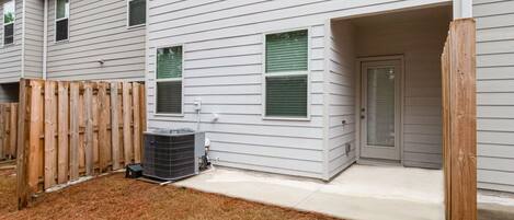 A residential building with a covered porch, a wooden fence, and an air conditioning unit.