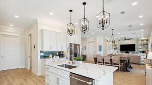 Une cuisine moderne avec des meubles blancs, un îlot central, des appareils en acier inoxydable et des luminaires suspendus.