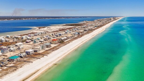 Vue aérienne d’une ville côtière avec une longue plage, des bâtiments et une jetée qui s’avance dans l’eau.