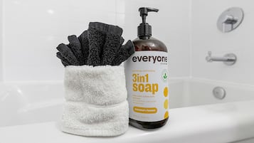 Un bagno con una vasca da bagno bianca, una bottiglia di sapone 3in1 e un asciugamano nero.