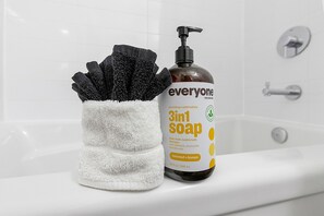 Een badkamer met een witte badkuip, een fles 3-in-1 zeep en een zwarte handdoek.
