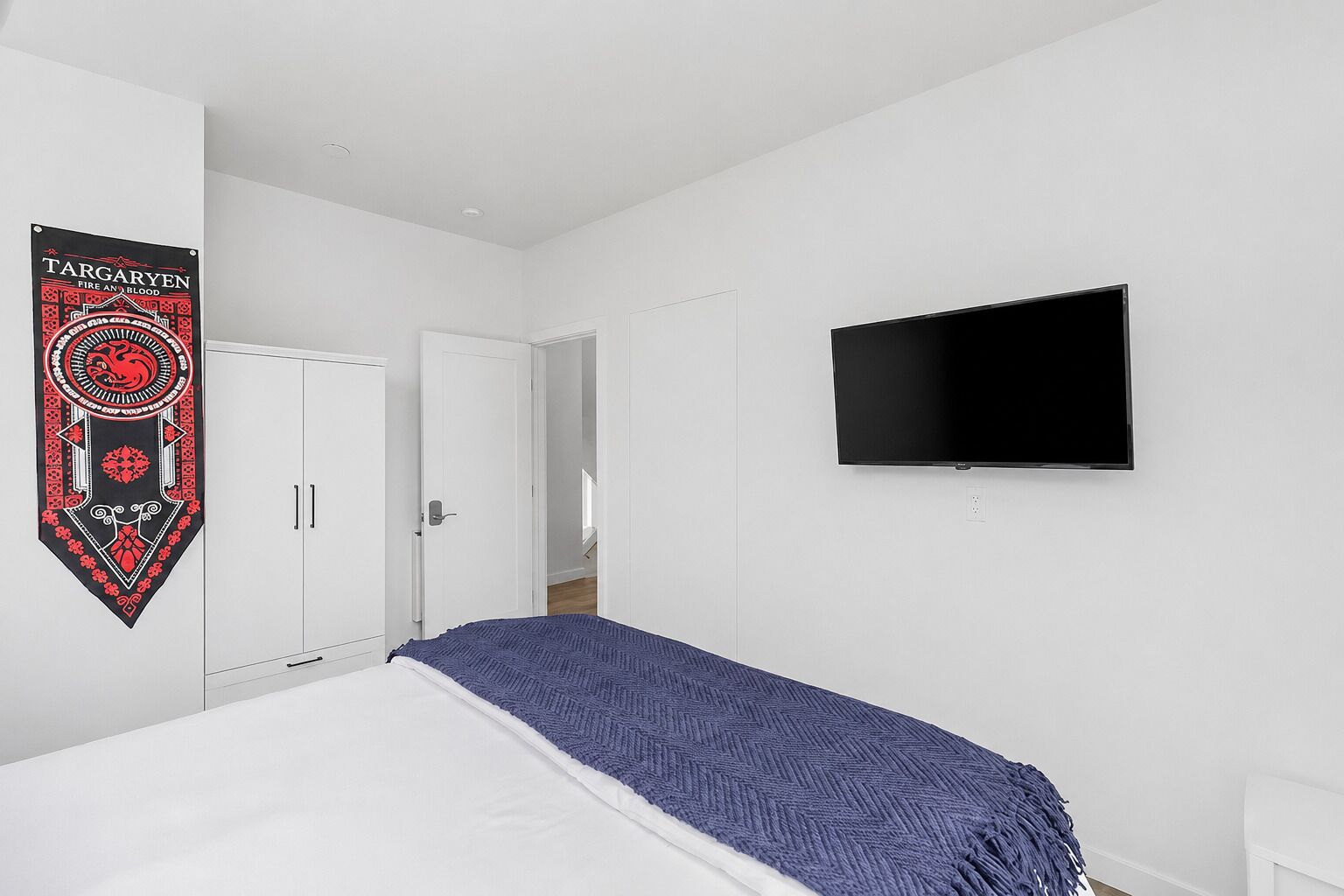 Quarto com uma cama, televisão fixada na parede e porta que dá para outro cômodo.
