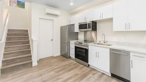 A modern kitchen with white cabinets, stainless steel appliances, and a wooden staircase. - Dreamfyre's Ancient Dragon Horn Suite (Seattle)