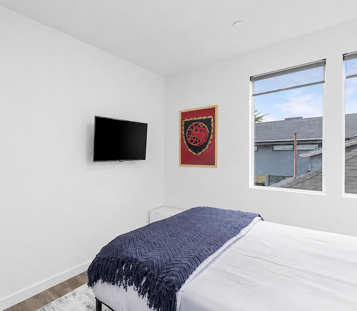 Quarto com cama, televisão, quadro e janela com vista para edifícios.