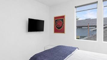 Quarto com cama, televisão, quadro e janela com vista para edifícios.