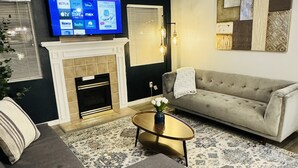 A living room with a fireplace, a sofa, a coffee table, and a flat-screen TV mounted above the fireplace displaying a Roku TV interface. - Charming 2-BHK Condo, nestled in the heart of picturesque Leavenworth. (Leavenworth)