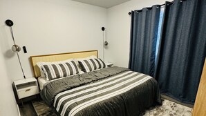 A bedroom with a bed, bedside tables, a nightstand, a ceiling fan, and a window with curtains. - Charming 2-BHK Condo, nestled in the heart of picturesque Leavenworth. (Leavenworth)