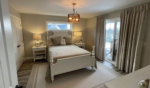 A bedroom with a large bed, two bedside tables with lamps, a window with curtains, and a view of the outdoors.
