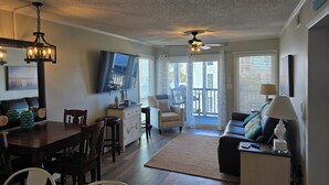 A spacious living area with a dining table, chairs, a sofa, and a TV mounted on the wall. - Seaside Retreat - Shore Drive, 3 bed, 2.5 bathrooms with an Ocean View. (Horry County)