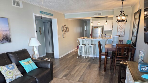 A modern living room with a dark leather sofa, a woven rug, and a dining area with a wooden table and chairs. - Seaside Retreat - Shore Drive, 3 bed, 2.5 bathrooms with an Ocean View. (Horry County)