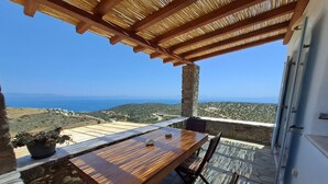 A wooden table and chairs on a stone patio with a view of the sea and hills. - Dorothea Panoramic Villa is one of a kind—a hidden gem  of Paros.Asteria (Paros)