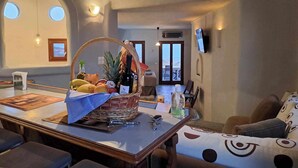 A dining area with a table set for two, a wicker basket with fruits and a bottle, and a view of the sea through the door. - Dorothea Panoramic Villa is one of a kind—a hidden gem  of Paros.Asteria (Paros)