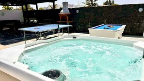 A hot tub with a table and chairs nearby, a stone wall, and a chimney in the background. - Stunning 3 Bed 2 Bath Villa in Playa Blanca (Yaiza)