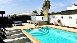A swimming pool with lounge chairs, a sunbed, and a small table. - Stunning 3 Bed 2 Bath Villa in Playa Blanca (Yaiza)