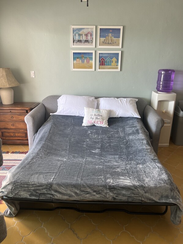 Une chambre à coucher comprenant un lit, des oreillers, une table de chevet, un distributeur d’eau et des œuvres d’art murales.