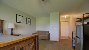 Une pièce avec un bureau en bois, un canapé, un réfrigérateur et des tableaux encadrés accrochés au mur.