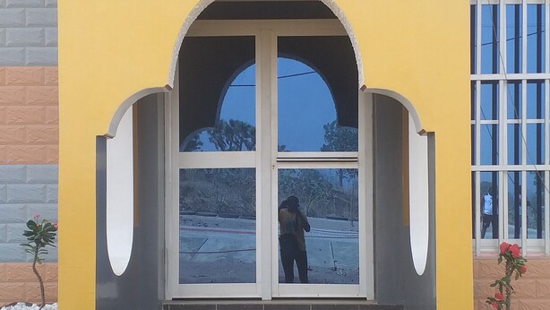 Fachada de hotel amarilla, cartel con el nombre y datos de contacto, y un conjunto de escaleras que conducen a la entrada.