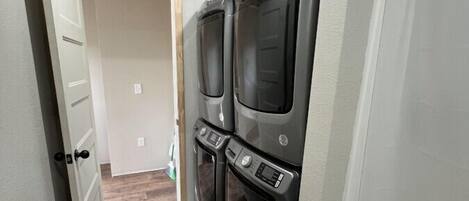 A laundry room with two stacked front-loading washers and dryers, wooden flooring, and a white door leading to another room.