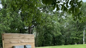 A wooden utility box with two gray electrical meters, a stone border, and a grassy area with trees in the background. - Nordin`s Escapes RV/Camper Site 1, near Lake Dardanelle, Mt. Nebo, and Mt. Petit Jean (Dardanelle)