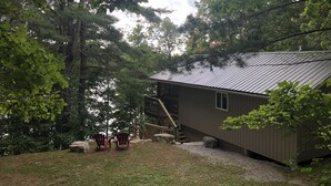 Un chalet rustique avec un toit en métal, entouré d’une forêt dense et bordé d’un chemin de gravier.