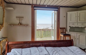 A bedroom with a bed, a wooden headboard, a nightstand, a white cabinet, a wooden chair, a menorah on a shelf, and a balcony with a view of the sea. - 3 bedroom pet friendly home in Källby (Källby)