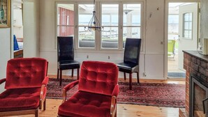 Een kamer met een houten vloer, een rode fluweelstoel, een zwarte stoel en een open haard.