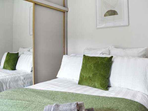 A hotel room with two beds, white bedding, green pillows, a green throw blanket, and a framed picture on the wall. - Escape to tranquility in our charming 2-bed cottage in Woodhead of Mailer. (Woodhead of Mailer)