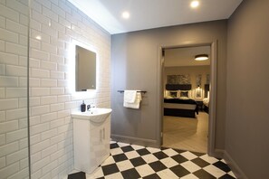 Een moderne badkamer met witte betegeling in metro-stijl, een witte wastafel en een zwart-wit schaakbordvloer.