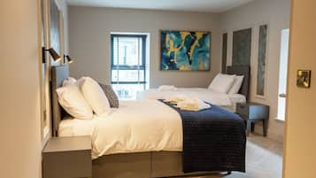 Une chambre d’hôtel avec deux lits, un grand tableau abstrait et une fenêtre avec des stores.