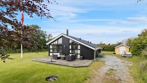 Une maison moderne dotée d’une grande terrasse, d’un garage séparé et d’une cour gazonnée.