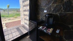 A stone-walled room with a coffee maker and snacks on a table, a view of a grassy area outside. - Estancia Cataviña Valle de Guadalupe (Valle de Guadalupe)