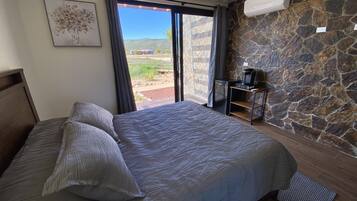 Ein Schlafzimmer mit Bett, einem kleinen Tisch mit Kaffeemaschine, einer Steinwand und Blick ins Freie.